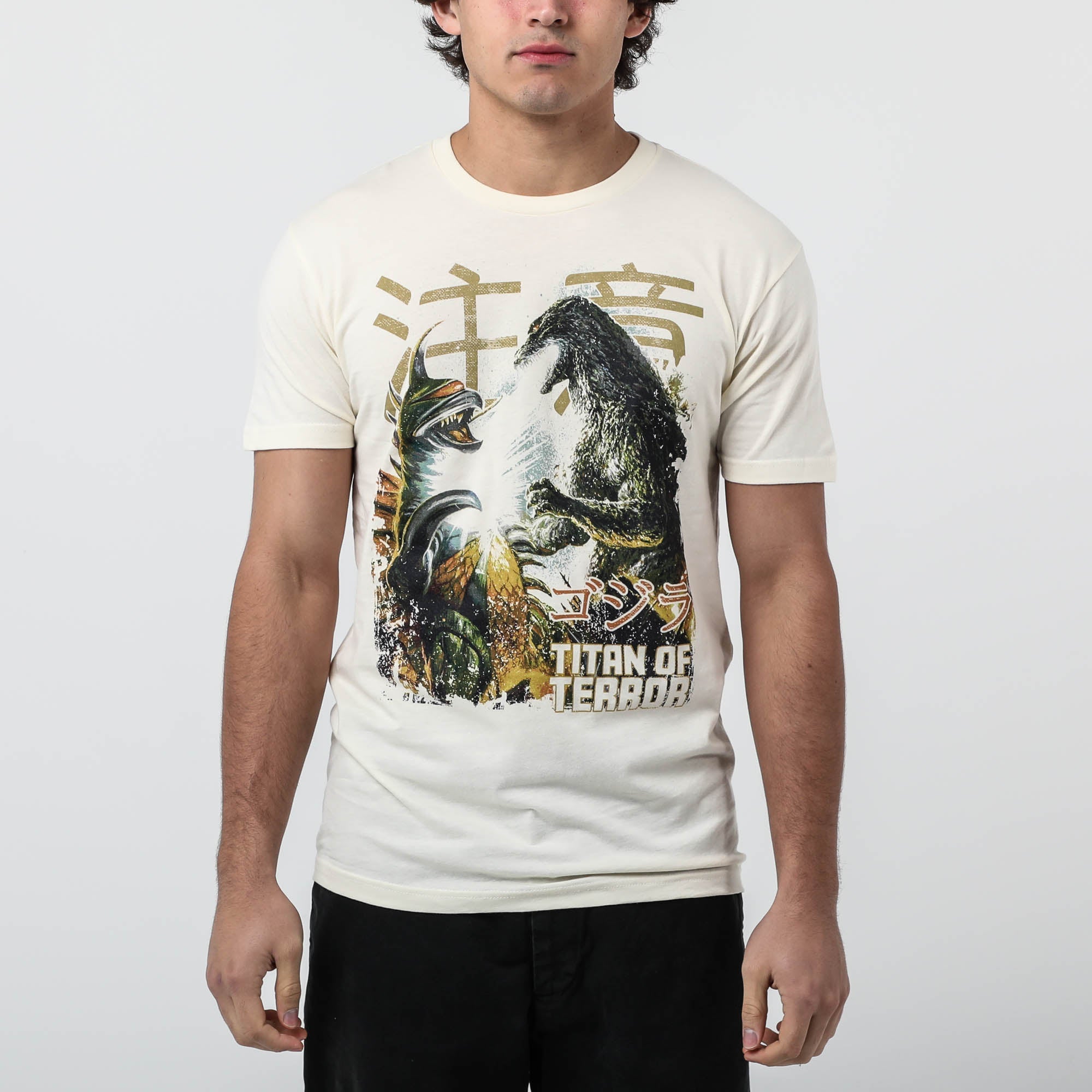 Male modeling Natural-colored T-shirt featuring a vintage-style graphic of Godzilla and Gigan in battle, with Japanese text and "Titan of Terror" lettering.